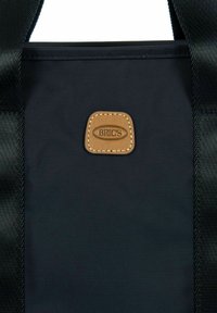 Borsa nera in nylon di forma rettangolare. Presenta una toppa con logo in pelle marrone con dettagli di cucitura e manici in tessuto nero.