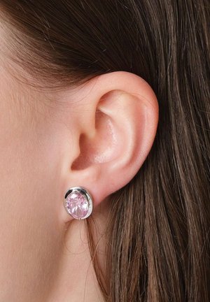 Nahaufnahme eines Frauenohrs mit glattem braunem Haar, das einen silbernen Ohrstecker mit großem rosa Edelstein trägt.