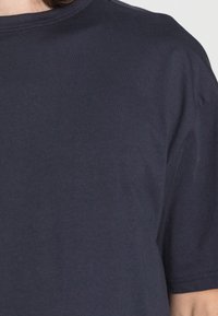 Tricou bleu marin realizat din bumbac moale, cu guler rotund și mâneci scurte, având o textură netedă și detalii de cusătură minime.