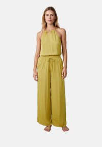 Conjunto amarillo sin mangas con cuello halter y detalle de ojal. Presenta una cintura elástica y pantalones anchos y fluidos. Textura suave.