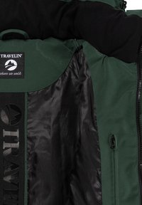 Groen en zwarte jak interieur met een ritszak, "TRAVELIN'" patch en gladde zwarte voering.