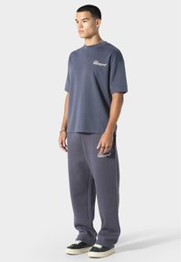 Grå oversized t-shirt og matchende sweatpants lavet af blødt stof, med et logo på brystet og benet i hvid. Sorte sneakers med cremefarvede såler.