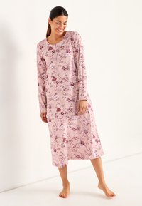 Långärmad nattskjorta i rosa tyg med ett blommönster i mörkare nyanser, med rundad halsringning och längd till mitt på vaden.