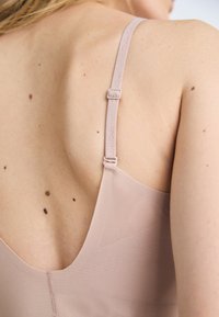Šviesiai rožinė liemenėlė su lygia tekstūra. Yra reguliuojamos petnešos ir žemas nugaros iškirpimas. Prekės ženklas matomas ant petnešos.