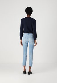 Tengerészkék pulóver, világoskék, slim fit farmernadrág és fekete cipő. A farmernadrág hátul zsebes, és kicsit rövidített a bokánál.