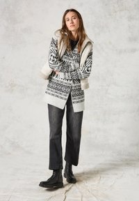 Svart och vit mönstrad stickad tröja med en krämfärgad huva, kombinerad med svarta jeans och svart lace-up kängor. Texturerade tygdetaljer synliga.