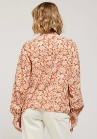Chemise à motif floral en orange rouille avec un design floral crème, à manches longues avec des poignets élastiques et un ourlet droit à l'arrière.
