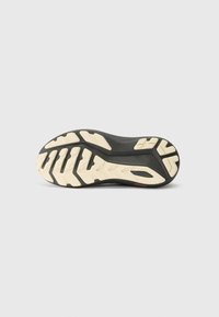 Semelle de chaussure en caoutchouc noir avec un relief blanc, présentant des motifs géométriques et des rainures pour l'adhérence. Design léger et flexible.