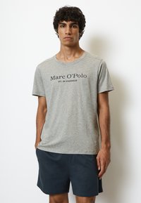 Graues Kurzarm-T-Shirt mit dem Aufdruck "Marc O'Polo EST. IN STOCKHOLM" in dunkler Schrift. Weicher Stoff, einfacher runder Halsausschnitt, lässige Passform.