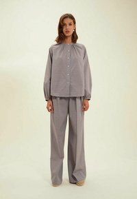 Ensemble en deux pièces à carreaux comprenant un haut ample avec un col froncé et des manches longues, associé à un pantalon large. Les couleurs disponibles incluent le bleu, le rose et le crème.