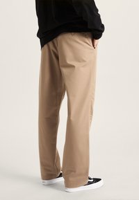 Pantaloni a gamba larga color khaki realizzati in misto cotone, con una texture liscia, tasche laterali e abbinati a sneakers nere.