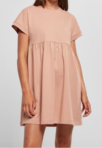 Kurzärmliges, locker geschnittenes Kleid aus weichem, rosa Baumwollstoff mit geraffter Taille, fließendem Rock und glatter Textur. Lässiges Design mit minimaler Ausstattung.