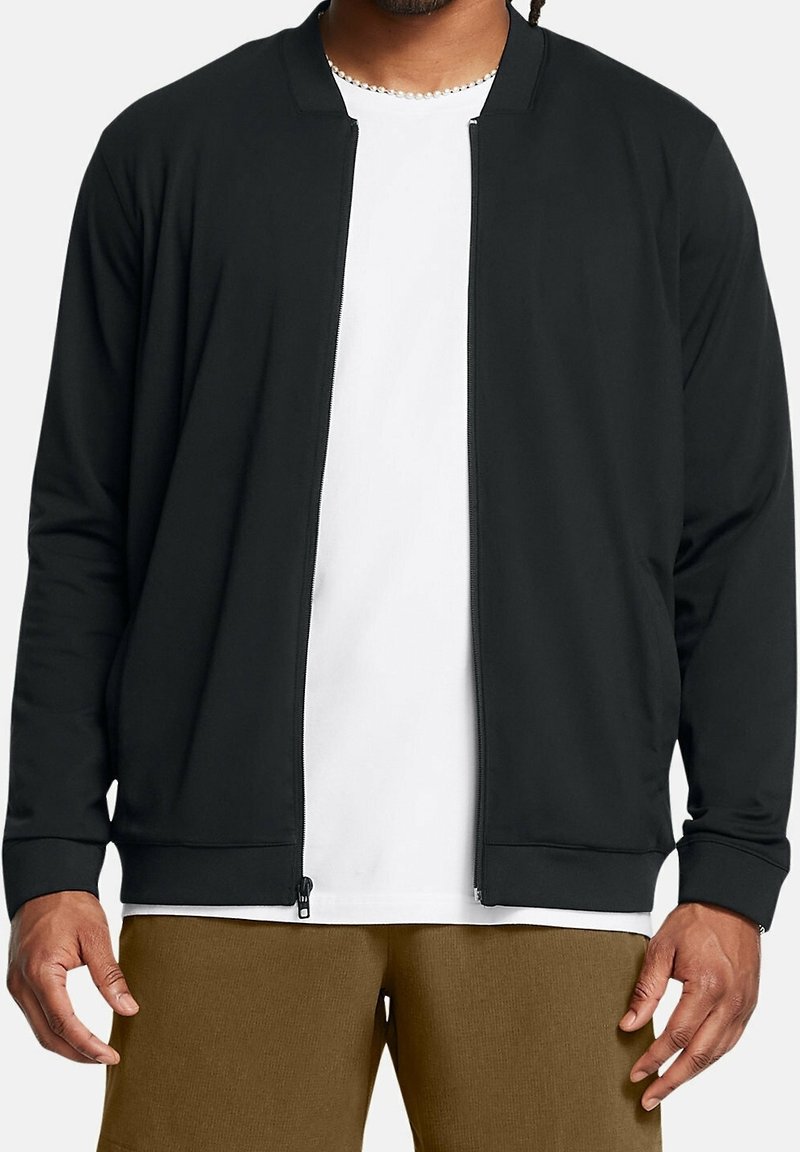 Veste noire zippée avec un col rond et des manches longues, fabriquée en tissu lisse. Comprend des poignets côtelés et un design minimaliste.