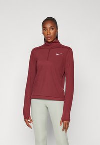 Burgundi sportfelső negyedcipzárral, hosszú ujjakkal és Nike logóval. Puha, sima anyag, testhez simuló kialakítással és magas gallérral.
