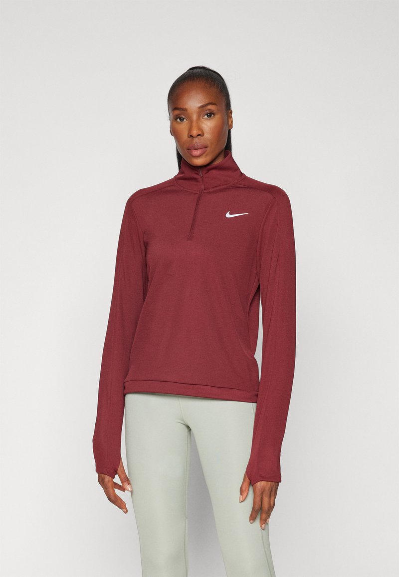 Burgundi sportfelső negyedcipzárral, hosszú ujjakkal és Nike logóval. Puha, sima anyag, testhez simuló kialakítással és magas gallérral.