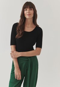 Haut noir à rayures avec des manches courtes et un col rond, associé à un pantalon vert taille haute avec un détail de ceinture nouée. Texture lisse.