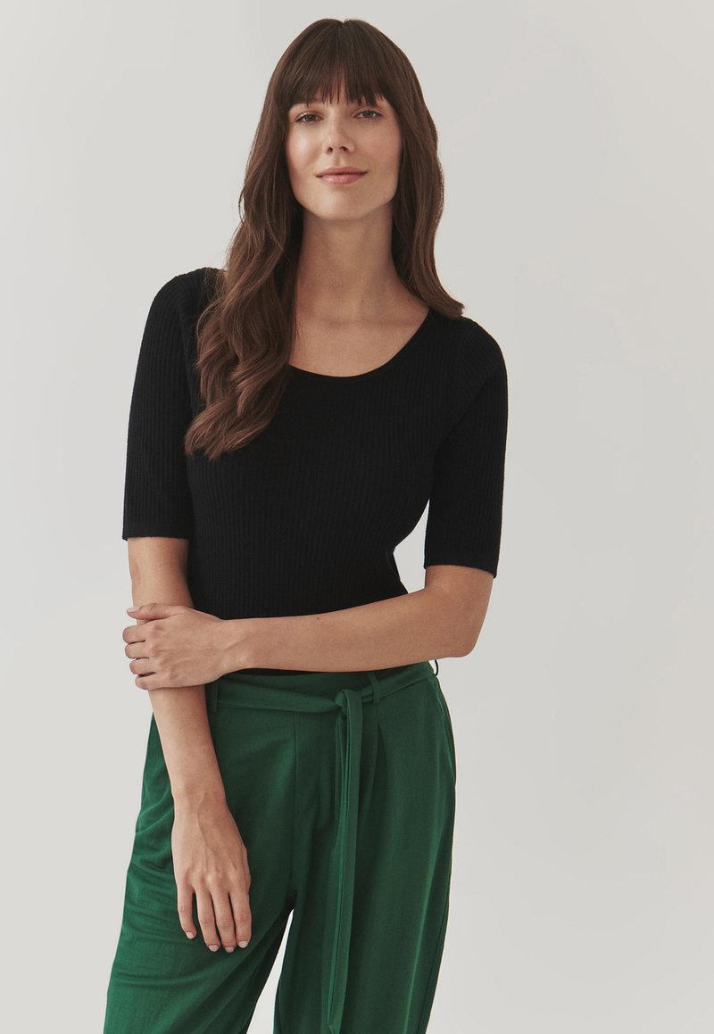 Haut noir à rayures avec des manches courtes et un col rond, associé à un pantalon vert taille haute avec un détail de ceinture nouée. Texture lisse.