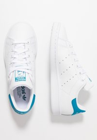 Weiße sportliche Sneakers aus glattem Leder mit blauen Akzenten an Ferse und Zunge sowie perforierten Details für bessere Atmungsaktivität.