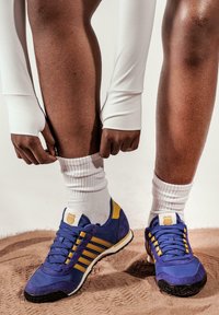 Baskets de sport bleu et jaune en matériaux en daim et en tissu. Les caractéristiques incluent trois bandes, une semelle texturée et un soutien de la cheville rembourré.