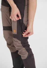 Bruine en donkergrijze wandelpantalon met een ritszak op de dij, met een gaasvoering, en een leren logo-opdruk.