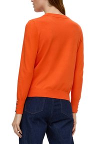 Oranges Pullover mit Rundhalsausschnitt, langen Ärmeln und geripptem Saum; hat Knopfakzente an den Ärmelbündchen und eine weiche Textur.