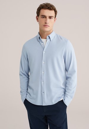 Lichtblauw overhemd met lange mouwen en knopen, met een subtiele textuur, voorzien van een standaardkraag en witte knopen, gecombineerd met een donkere broek.