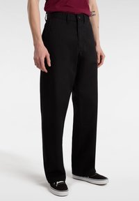 Pantaloni neri dalla vestibilità comoda, realizzati in morbido cotone. Presentano una chiusura con bottone e tasche laterali, abbinati a sneakers nere.