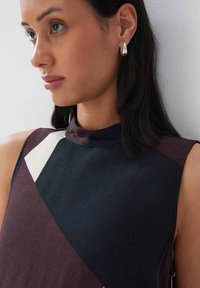 Ärmelloses Top mit hohem Kragen, das geometrische Abschnitte in Dunkelblau, Kastanienbraun und Weiß aufweist. Glatte Textur; minimalistisches Design.