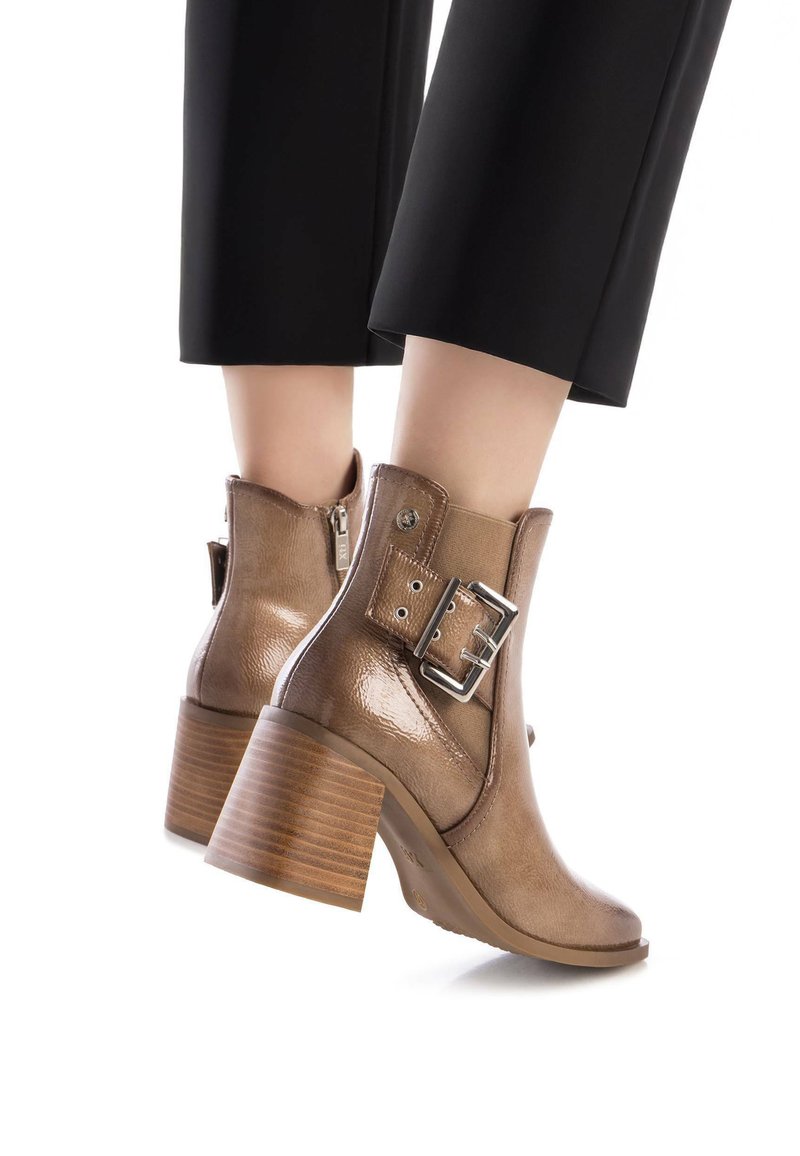 Botas de tobillo de cuero marrón con un acabado brillante, acento de hebilla de metal y tacón cuadrado, combinadas con pantalones negros cropped.