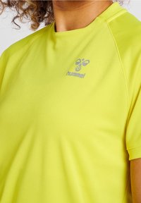 Lätt kortärmad skjorta i stark gult, med en jämn textur och en reflekterande logotyp. Sömlös design runt halsen och axlarna.