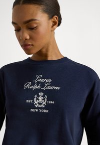 Μπλε φούτερ με στρογγυλή λαιμόκοψη, διακοσμημένο με άσπρο κεντητό κείμενο: "Lauren Ralph Lauren," "EST. 1996," και "ΝΕΑ ΥΟΡΚΗ." Κανονική εφαρμογή.