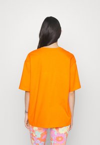 Jasně oranžové oversized tričko s kulatým výstřihem a krátkými rukávy. Látka je hladká, bez viditelných vzorů nebo zdobení.