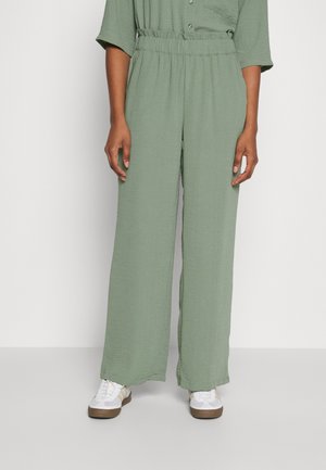 Pantalons larges vert clair en tissu texturé avec une taille élastique et des plis légers. Associés à des baskets blanches.