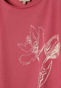 Tissu rose avec un motif floral en lignes blanches présentant de grands pétales et des feuilles allongées sur un vêtement de petite taille.