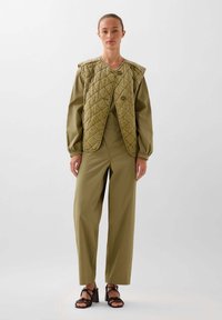 Olijfgroene gewatteerde vest met een ronde hals en knopen aan de voorkant, gedragen over een bijpassende outfit bestaande uit losse broek.