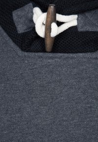 Maglione grigio con una texture morbida, caratterizzato da un pannello in maglia nera, un cordino bianco e una chiusura con toggle in legno.