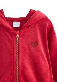 Rød fleece-hoodie med en guldfarvet lynlås og et lille broderet hjerte på venstre side. Blød tekstur og hætte.