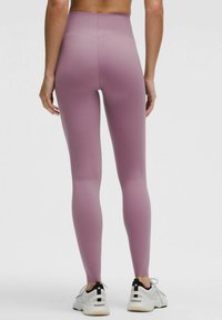 Kõrge talje ja keha lähendavad retuusid pehmest lillasest kangast. Sile tekstuur koos õmbluste detailidega, koos valgete tossudega.