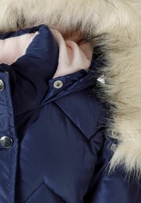 Veste matelassée marine avec une capuche en fausse fourrure, doublure en polaire rose et boutons-pression argentés. Texture matelassée en forme de losange sur tout le tissu.