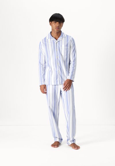 Sininen ja valkoinen raidallinen puuvillapijama-asuste; napitettava paita, jossa on tasku, ja matching-housut suorilla lahkeilla, pehmeä pinta ja rento muotoilu.