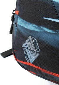 Mochila negra y azul con un logo geométrico, que presenta franjas diagonales rojas y turquesa, y una superficie de tejido texturizado.