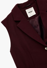 Burgunderfarbenes ärmelloses Blazer mit einem Reverskragen, silbernem Knopfdetail und glatter Textur. Das Innenfutter hat einen passenden Stoff.