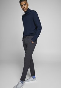 Marineblå turtleneck sweater parret med lysegrå mønstrede bukser og grå sneakers med blå sokker. Glat tekstur, tætsiddende design.