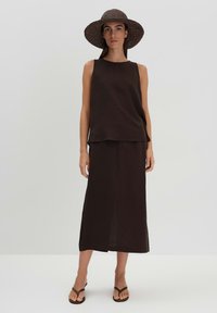 Completo top senza maniche e gonna marrone, caratterizzato da una vestibilità comoda e una texture morbida. Abbinato a un cappello intrecciato a tesa larga e sandali marroni.