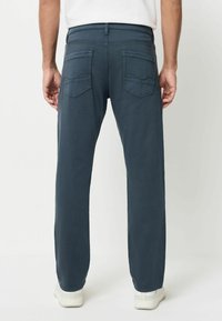 Sötétkék, egyenes szabású nadrág, két hátsó zsebbel és sima felülettel, fehér sportcipővel párosítva.