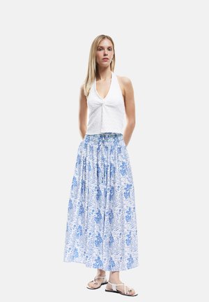 Hvid halterneck top med snoet frontdetalje, parret med en lang, blå blomstermønstret nederdel. Modellen har flade sandaler på.