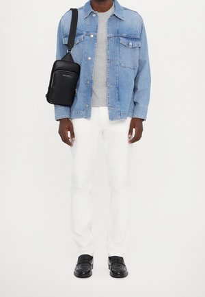 Veste en jean bleu clair, t-shirt gris à col rond, pantalon slim blanc, et sac bandoulière noir. Des mocassins noirs complètent la tenue.