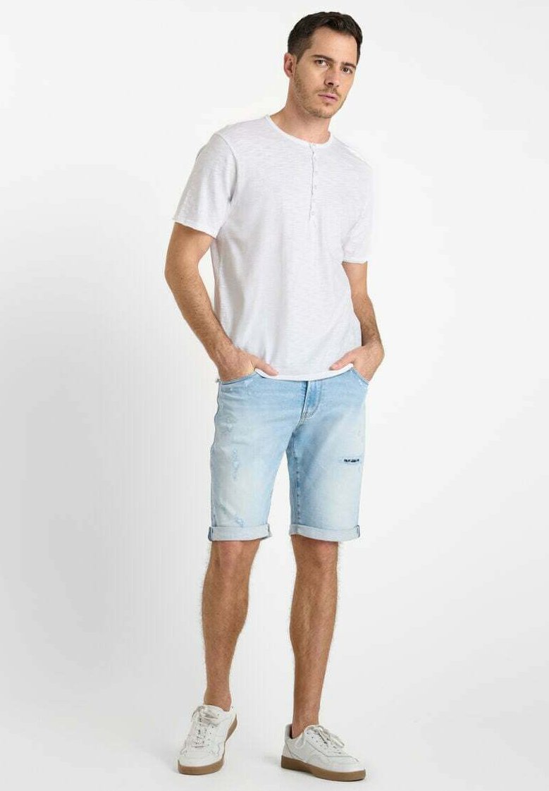 Lichtgrijze kortekraagshirt met een henley-halslijn, gecombineerd met lichtblauwe spijkerbroekshorts met opgerolde zomen en versleten details. Witte sneakers.