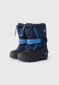 Botas de nieve aisladas de color azul marino con suela de goma negra, cordón ajustable y acentos azules. Presenta la marca "SOREL" en el lateral.