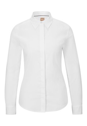 Chemise blanche à manches longues, en coton crisp, avec un col classique, une patte de boutonnage à l'avant et une coupe ajustée. Texture lisse, sans motifs.